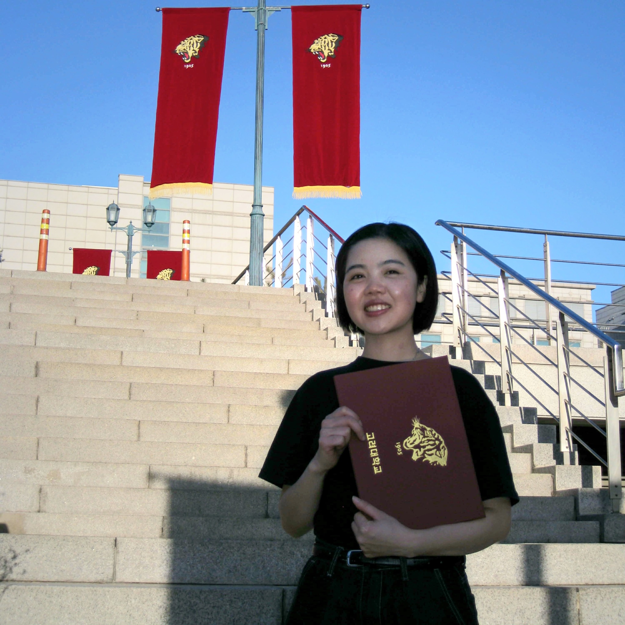 Trinh holding her diploma on the steps at Korea University